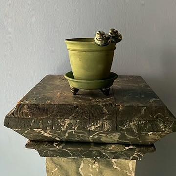 Green pot with decorative elements on a wooden pedestal against a plain wall