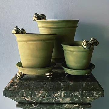 Set of three green ceramic pots with decorative feet on a marble base against a light blue wall.