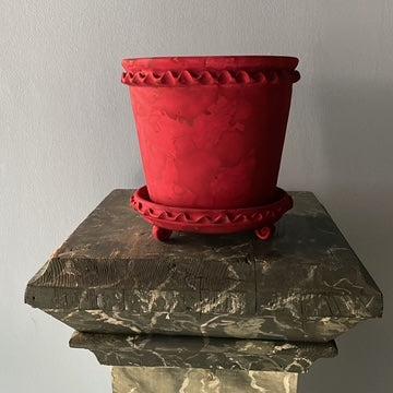 Red pot with decorative rim on a stone surface against a plain background