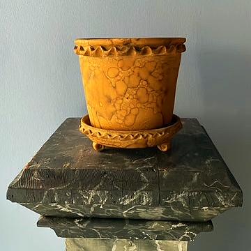 Decorative yellow pot with intricate designs on a stone pedestal against a plain background
