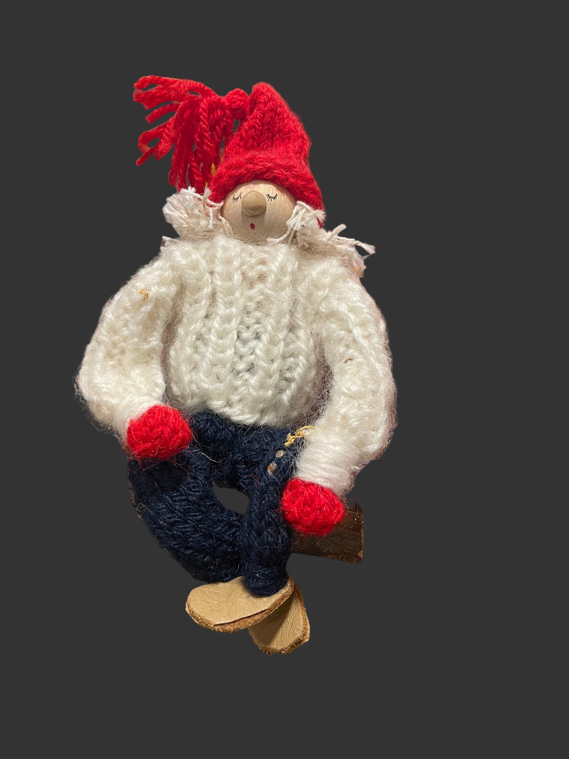 Knitted gnome with a red hat and white sweater on a dark background