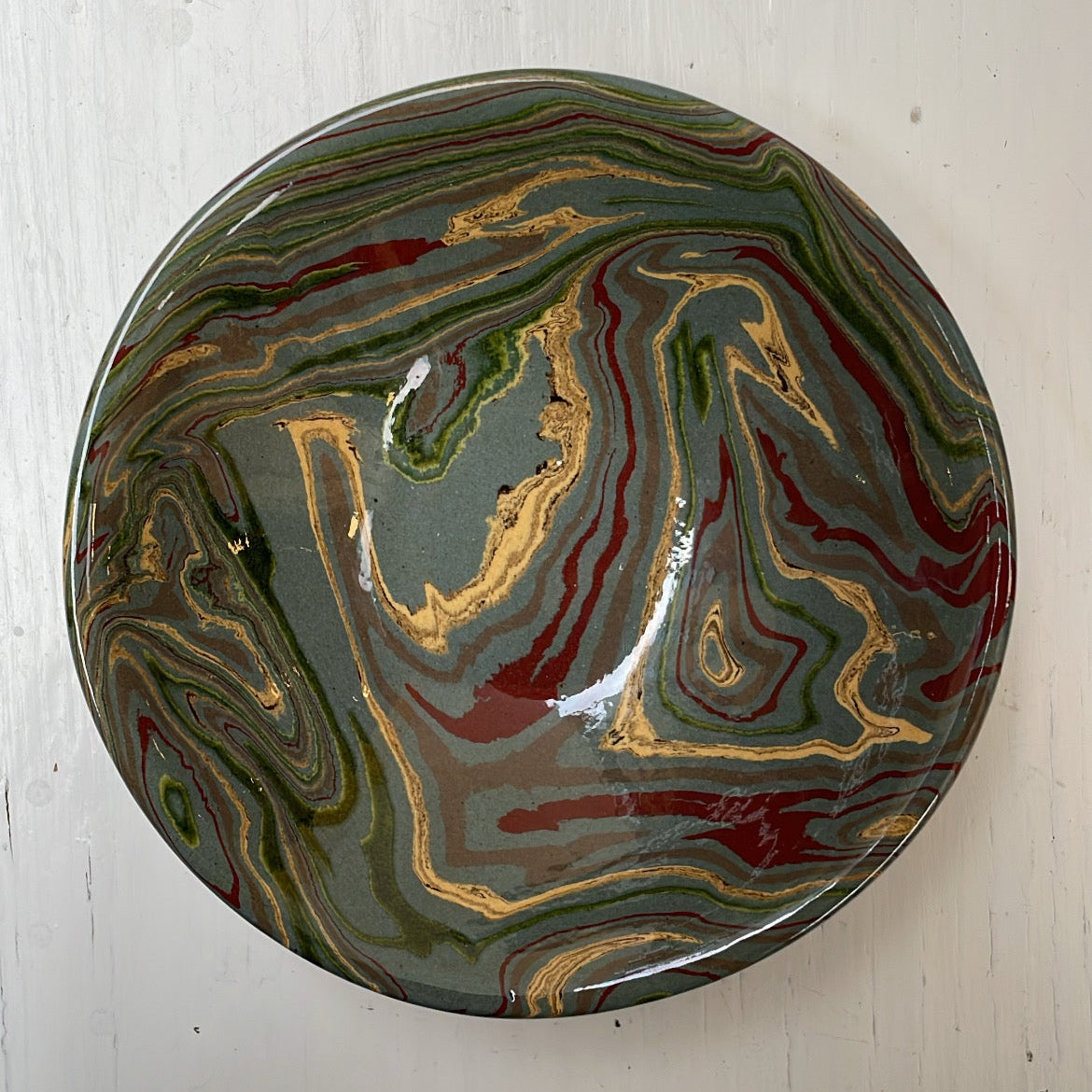 Decorative ceramic plate with marbled design on a white wooden surface
