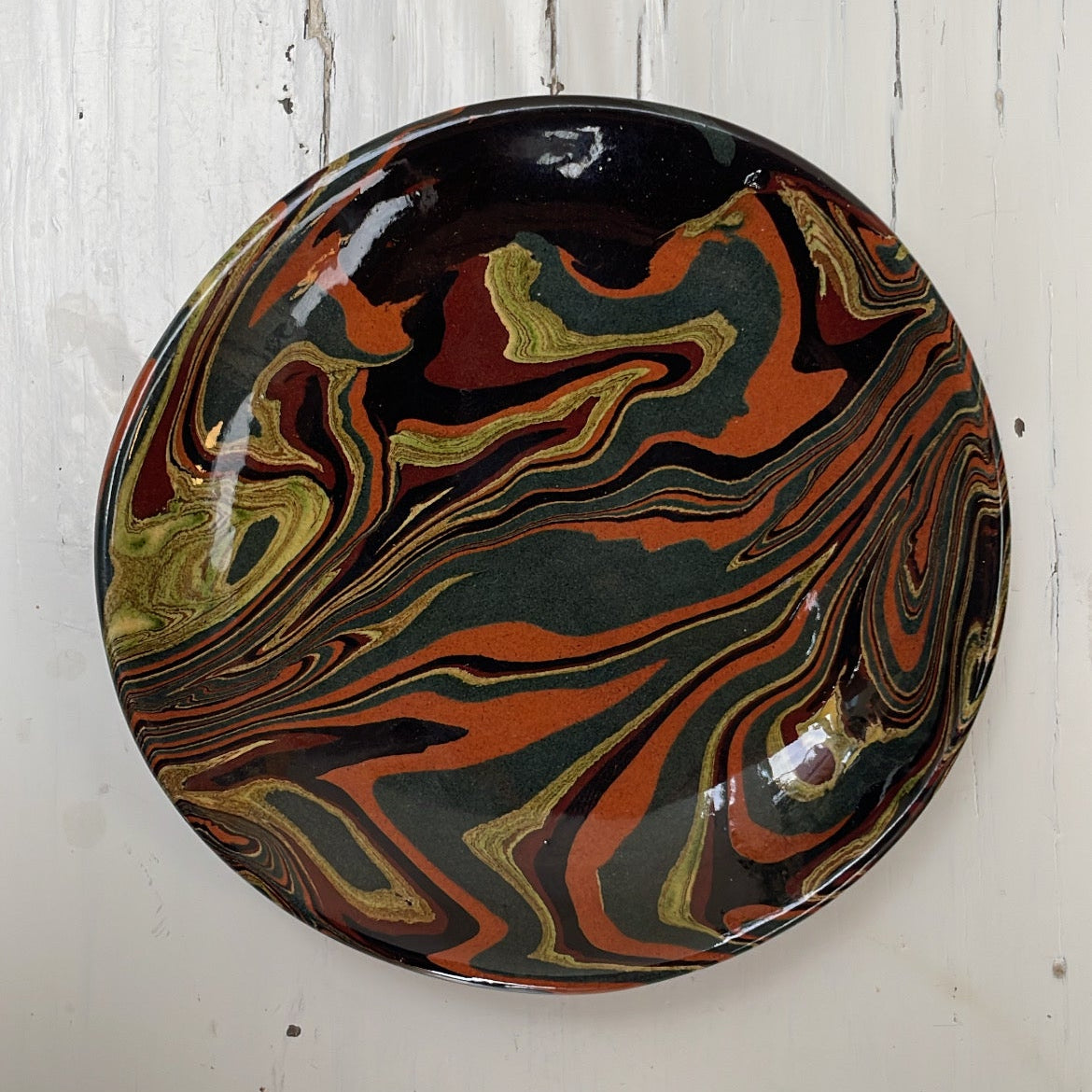 Marbled ceramic plate with black, red, and gold colors on a white wooden background