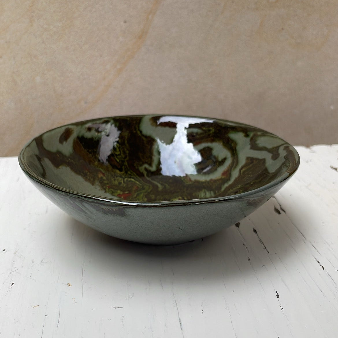 Green ceramic bowl on a white surface with a beige background