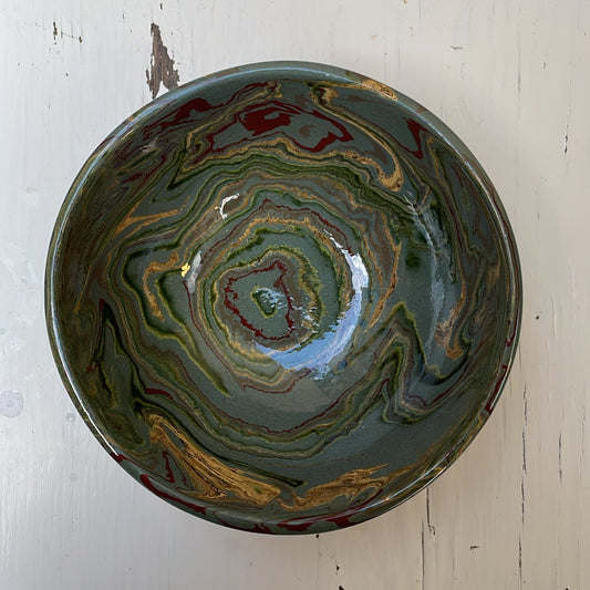 Decorative ceramic bowl with swirling green and gold pattern on a white wooden surface