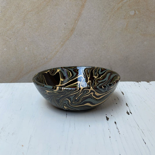 Small ceramic bowl with black and gold patterns on a white surface with a beige background