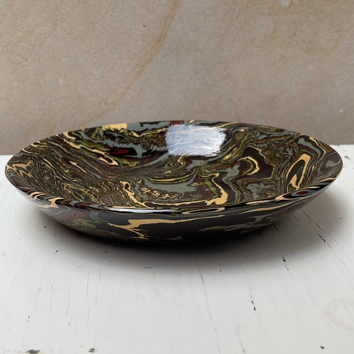 Decorative ceramic plate with gold and black marbled design on a white surface.